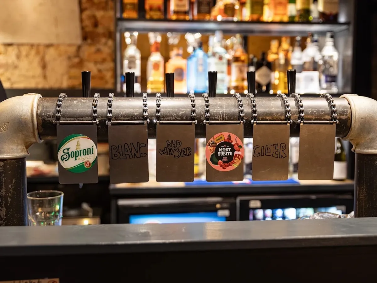 Csavaros acélcsőre épített csapsor, kézzel írt táblákkal: Soproni, Blanc, Budweiser, Mort Subite, Cider