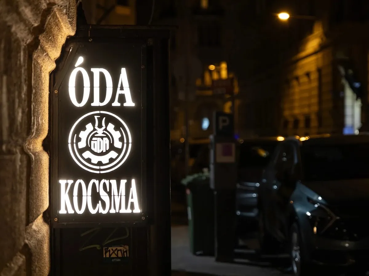 Az ÓDA KOCSMA világító utcai táblája éjszaka, a bejárat kőfalán